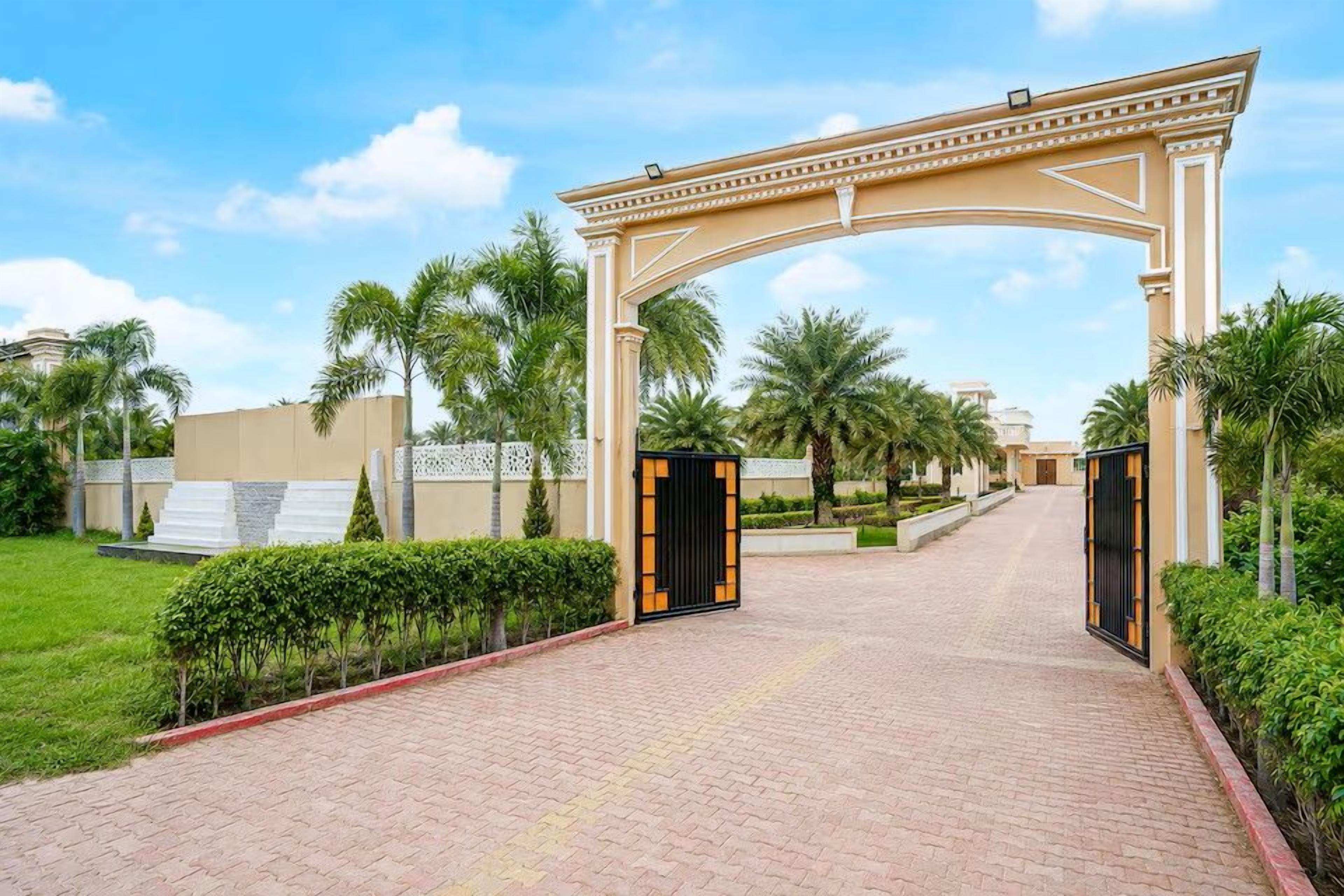 A gated entrance with a decorative archway, paved pathway, and palm trees.