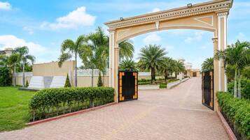 A gated entrance with a decorative archway, paved pathway, and palm trees.