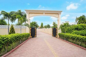 A paved pathway leading to a gated entrance with a decorative archway, flanked by neatly trimmed hedges and palm trees. - Amar Resorrt Motihari Bihar (Motihari)