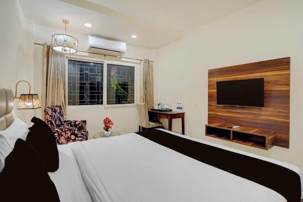 Habitación de hotel con cama, escritorio, silla, televisor montado en un panel de madera y equipo de aire acondicionado.