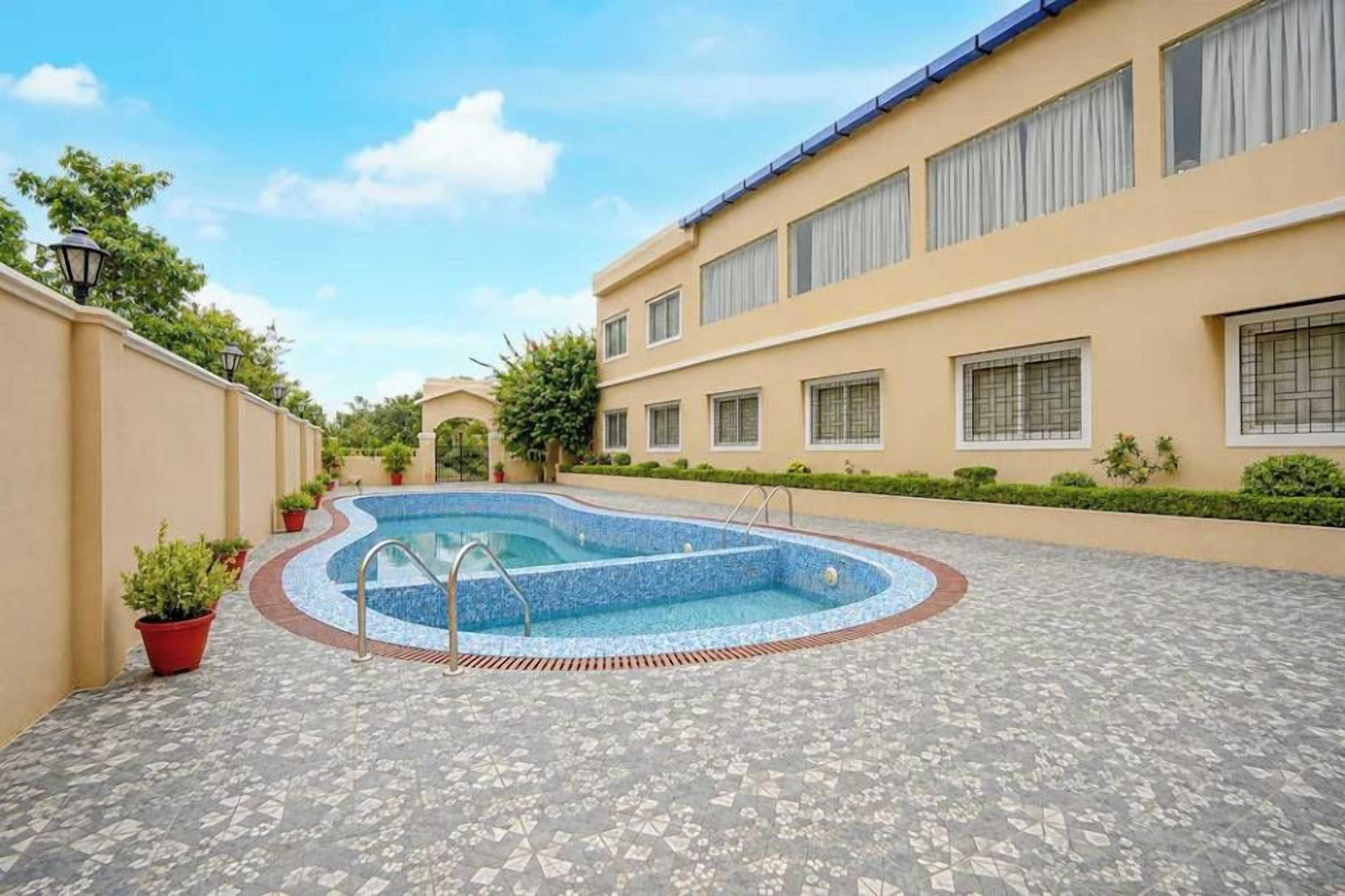 A swimming pool with a tiled deck, surrounded by a building with multiple windows and a flat roof.