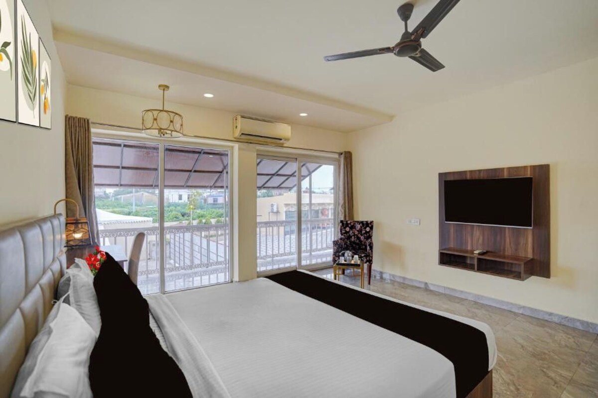 A hotel room with a bed, a TV mounted on the wall, a ceiling fan, and a balcony with a view.