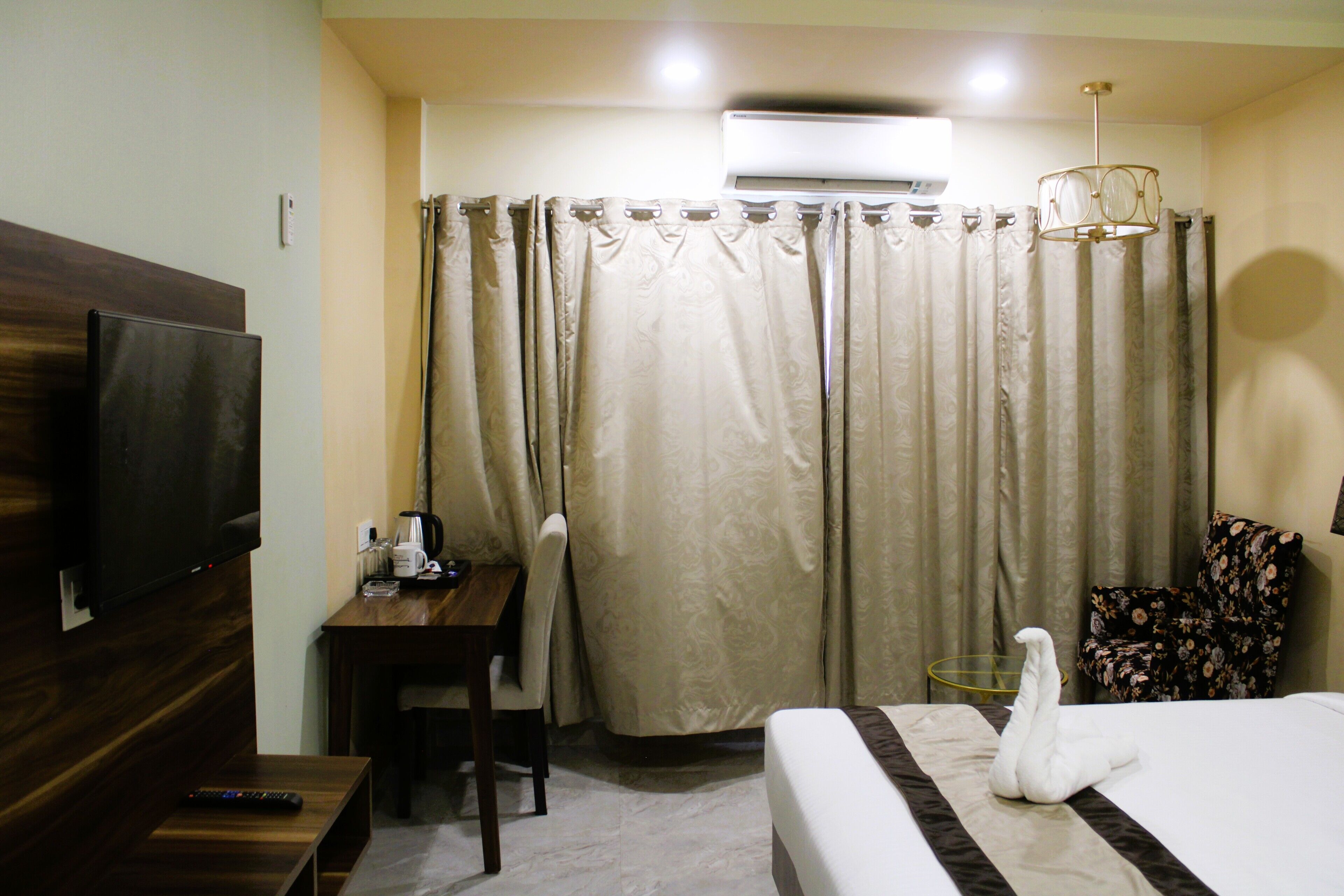 A hotel room with a bed, a TV, a desk, a chair, and a curtain.