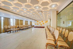 A conference room with rows of chairs, a hexagonal ceiling design, and large windows with curtains. - Amar Resorrt Motihari Bihar (Motihari)