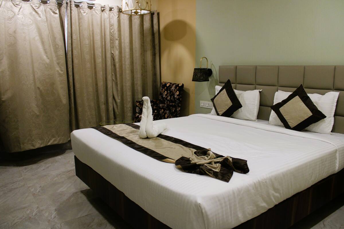 A neatly made bed with a towel and a robe, a headboard with pillows, a wall-mounted lamp, and a curtain.