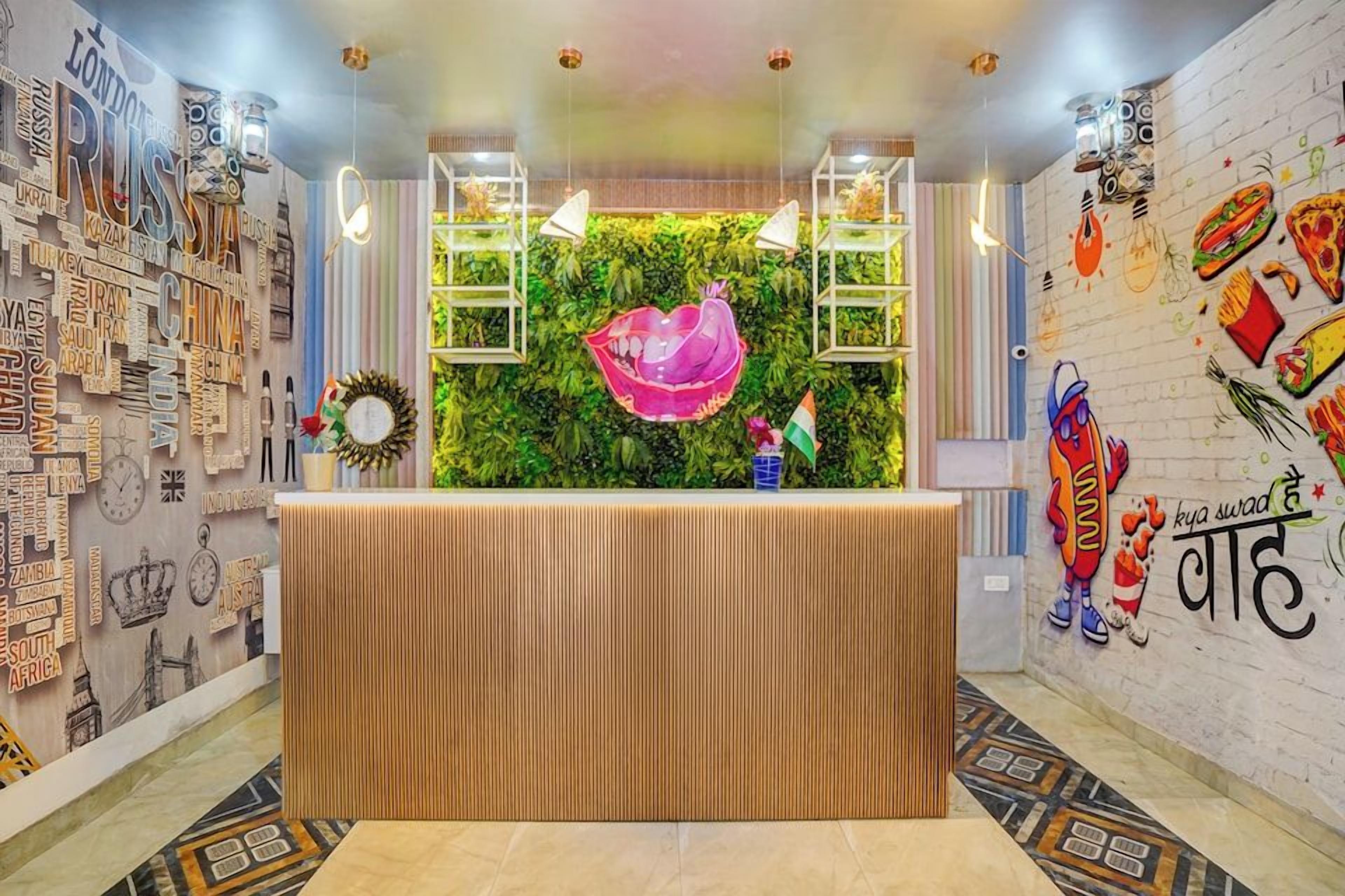 A reception area with a wooden reception desk, a green wall with a pink decorative element, and a wall with various international city names and food illustrations.