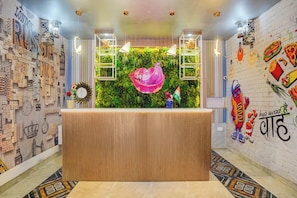 A reception area with a wooden reception desk, a green wall with a pink decorative element, and a wall with various international city names and food illustrations. - Amar Resorrt Motihari Bihar (Motihari)