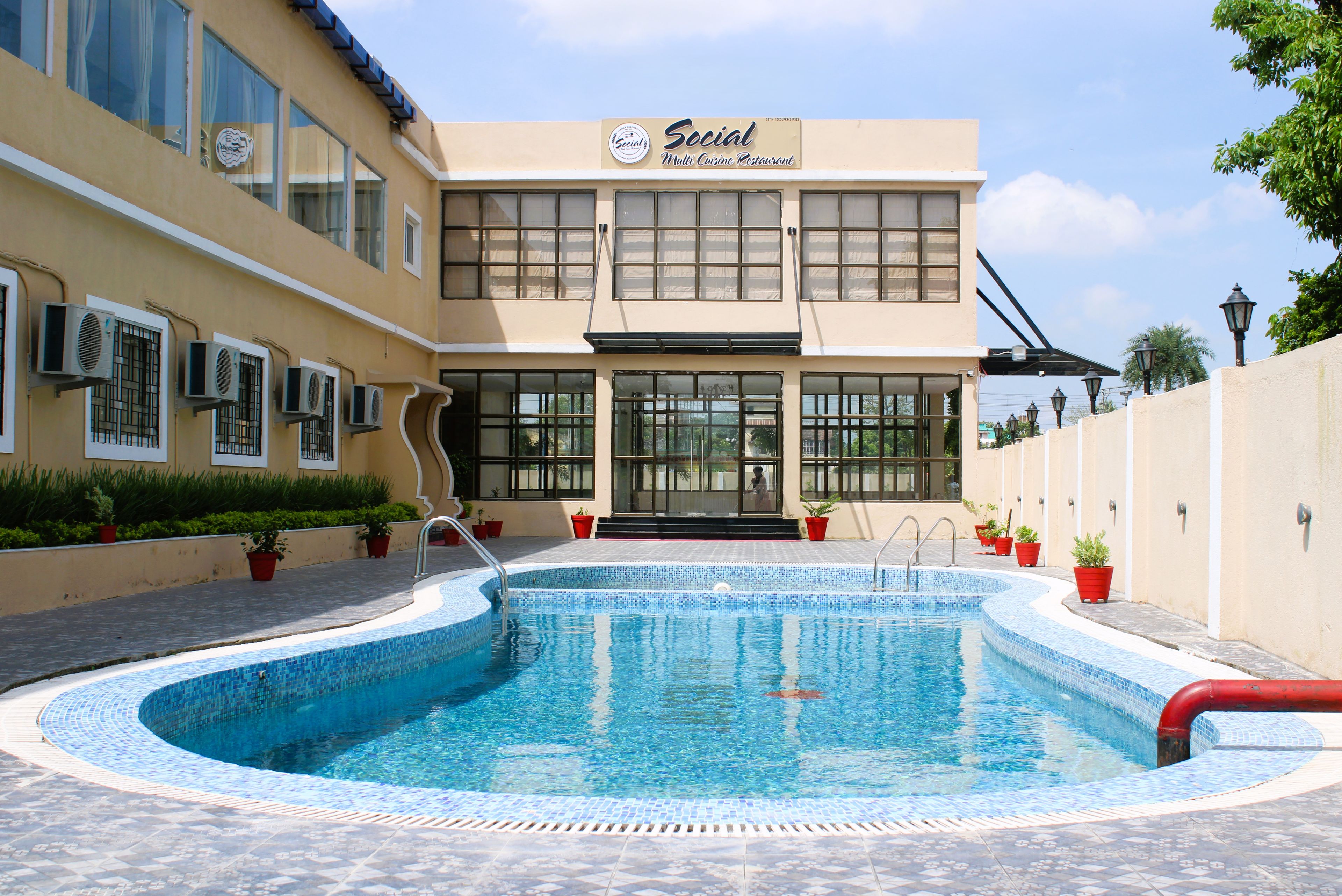 A building with a sign reading 'Social Multi Cuisine Restaurant' and a swimming pool with a tiled edge.