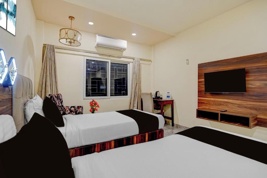 A hotel room with two beds, a TV mounted on the wall, an air conditioning unit, and a window with curtains.
