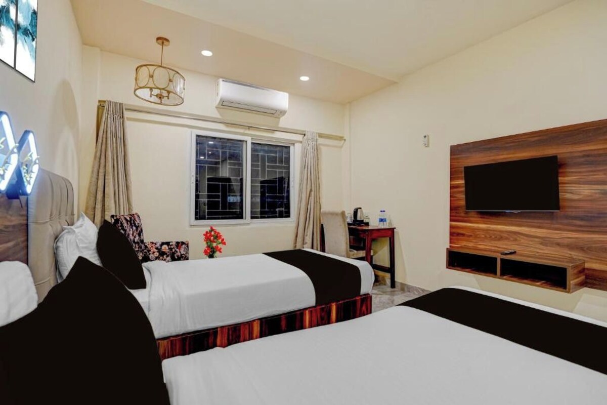 A hotel room with two beds, a TV mounted on the wall, an air conditioning unit, and a window with curtains.
