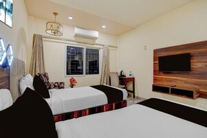 Habitación de hotel con dos camas, un televisor montado en la pared, aire acondicionado y una ventana con cortinas.