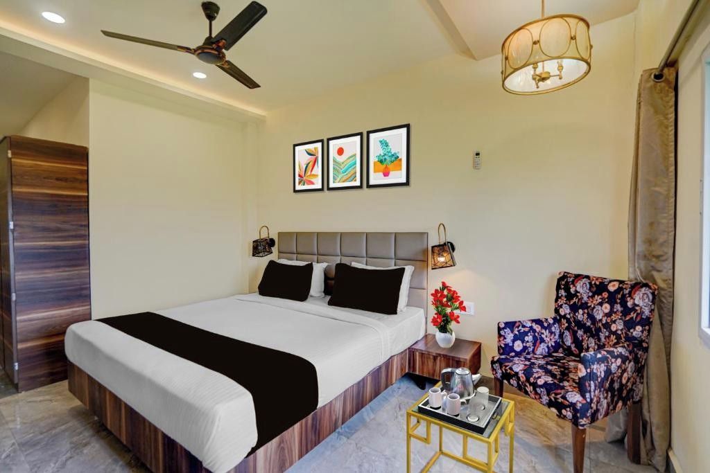 A hotel room with a bed, a chair, a small table with a tray, a ceiling fan, and wall-mounted artwork.