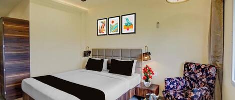 A hotel room with a bed, a chair, a small table with a tray, a ceiling fan, and wall-mounted artwork.