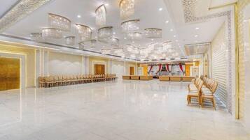 A spacious hall with rows of chairs, a stage with a red curtain, and multiple chandeliers.