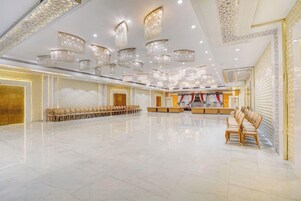 Un amplio salón con filas de sillas, un escenario con cortina roja y múltiples candelabros.