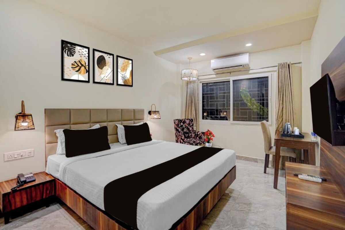 A hotel room with a large bed, a desk, a TV, and artwork on the wall.
