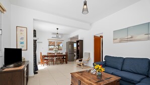 Una sala de estar con un sofá, una mesa de centro con flores, un televisor y un mueble de madera.