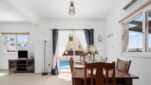 Comedor con mesa dispuesta para cuatro, piscina visible a través de un ventanal y un ventilador de techo.