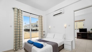 Un dormitorio con cama, mesita de noche, televisor y balcón con cortinas.