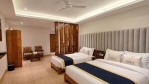 A hotel room with two beds, a desk, chairs, a wooden partition, and a ceiling fan.