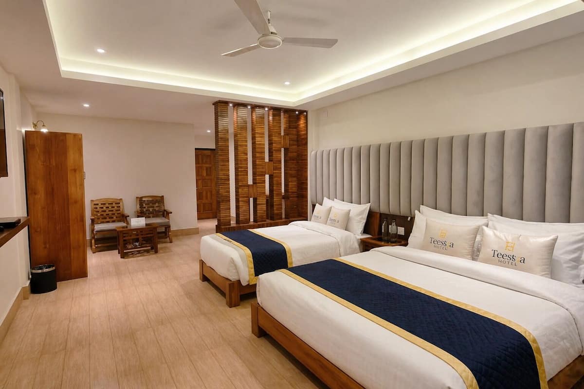 A hotel room with two beds, a desk, chairs, a wooden partition, and a ceiling fan.