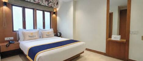 A hotel room with a bed, a bedside table with a phone, a mirror, and a door.