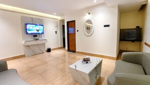 A modern living room with a flat-screen TV, a wooden door, a round mirror, and a small table with a magazine.
