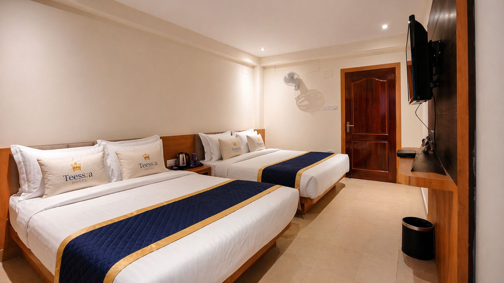 A hotel room with two beds, a television, a wooden door, and a trash can.