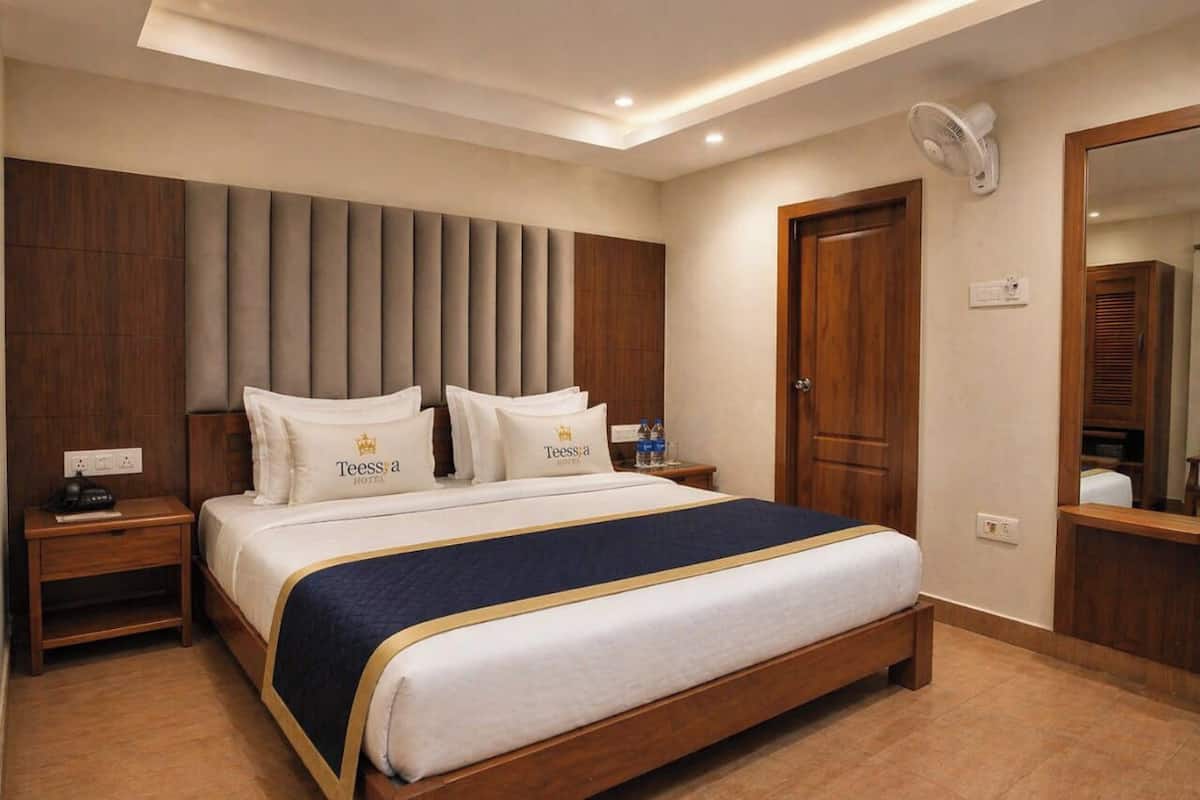 A hotel room with a bed, bedside tables, a mirror, and a wall-mounted fan.