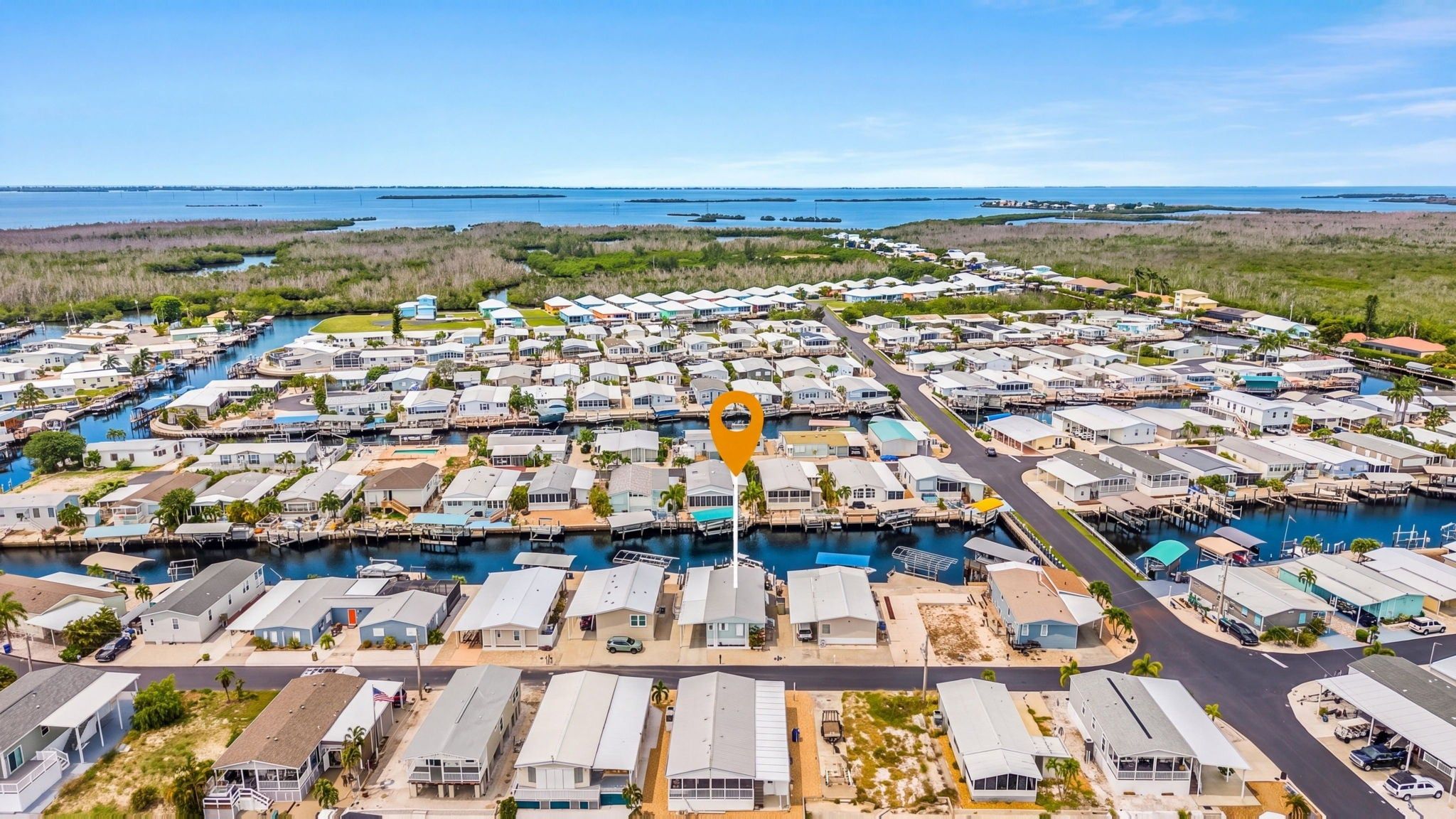 A marina with numerous boats docked, surrounded by a residential area with houses and a clear view of the ocean.