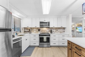 A modern kitchen with white cabinetry, a stainless steel refrigerator, a microwave, and an oven. - The Reel Escape! St. James City 2/2 with Boat Lift! (Saint James City)