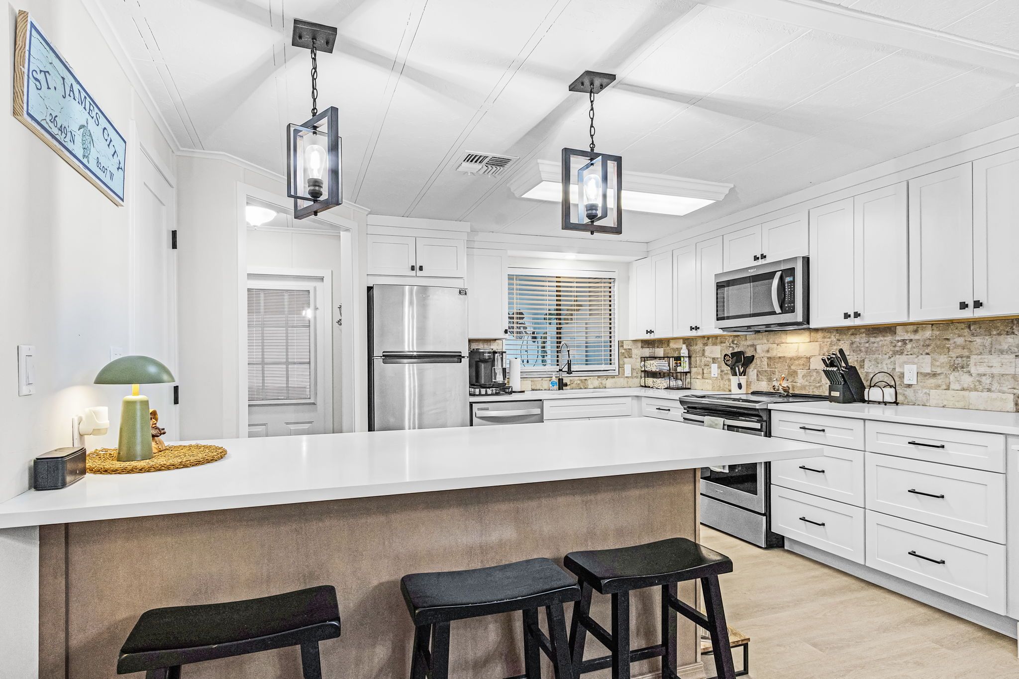 A modern kitchen with white cabinetry, stainless steel appliances, and a large island with bar stools.