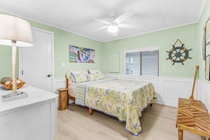 Ein Schlafzimmer mit einem Bett, einem Deckenventilator, einem Fenster mit Jalousien, einem an der Wand befestigten Schiffslenker und einem kleinen Tisch.