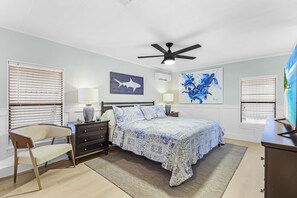 Ein Schlafzimmer mit einem Bett, Nachttischen, einem Sessel, einem Deckenventilator und Kunstwerken an den Wänden.