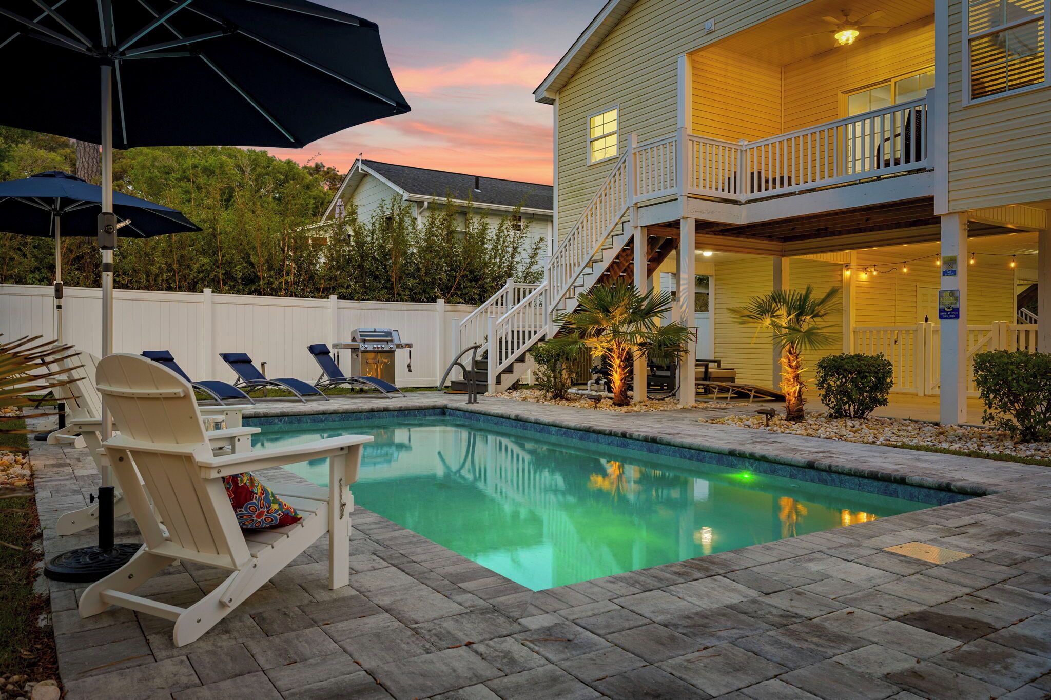 A backyard with a swimming pool, lounge chairs, and a covered patio area.