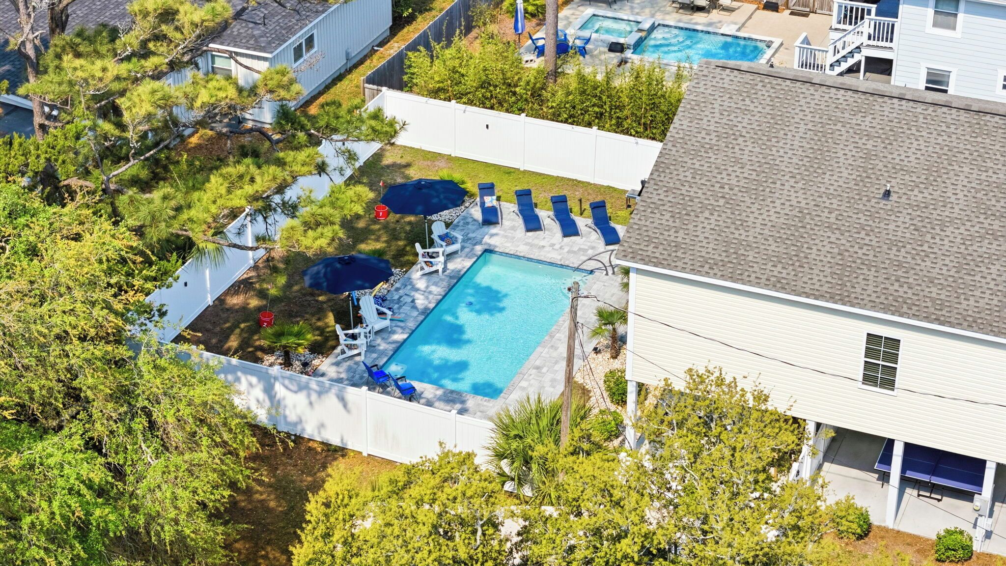 A residential backyard with a swimming pool, lounge chairs, and a tennis court.