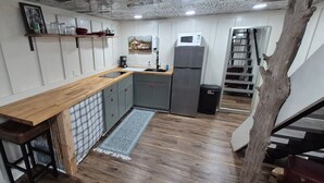 Een keuken met een houten aanrecht, grijze kastjes, een magnetron en een koelkast.