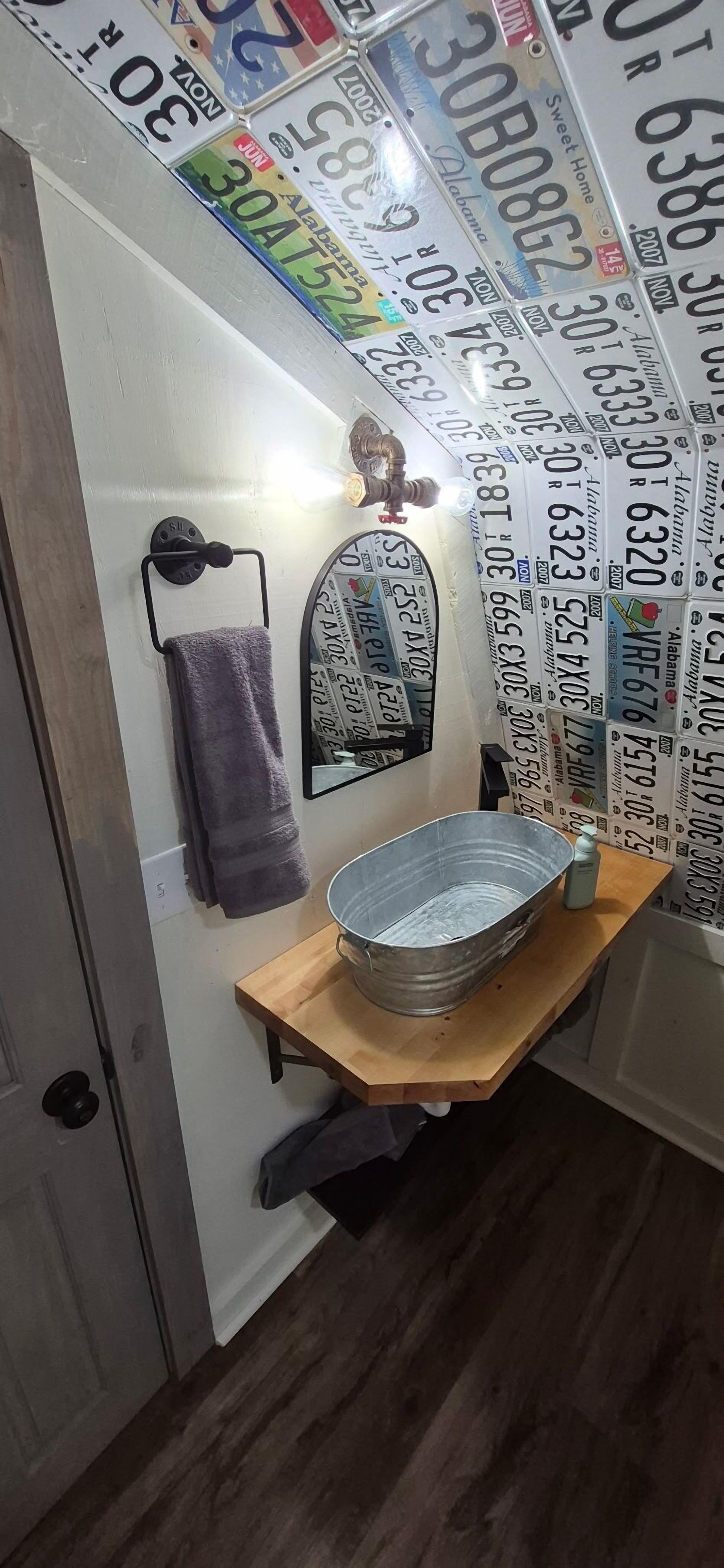 Ein Badezimmer mit einem Metallwaschbecken, einem Handtuchhalter mit einem violetten Handtuch und einer Wand mit Autokennzeichen.