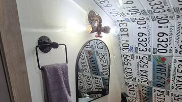 Ein Badezimmer mit einem Metallwaschbecken, einem Handtuchhalter mit einem violetten Handtuch und einer Wand mit Autokennzeichen.