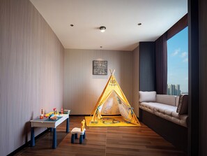 Ein modernes Zimmer mit Blick auf eine Stadtlandschaft, eine Couch, ein Tisch mit Spielzeug und ein gelbes Zelt.
