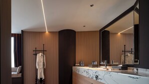 Un baño moderno con lavamanos de mármol, paneles de pared de madera, un espejo grande y un perchero para toallas.