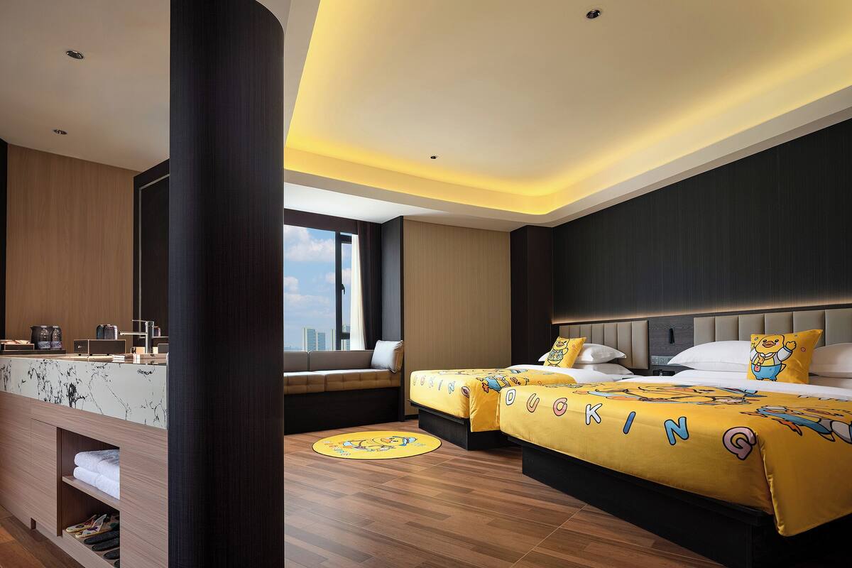 A modern hotel room with a large bed, a sofa, a desk with a computer, and a view of the city.