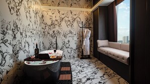 Un baño moderno con pared de mármol, una bañera, una zona de estar con vistas y un perchero para bata.