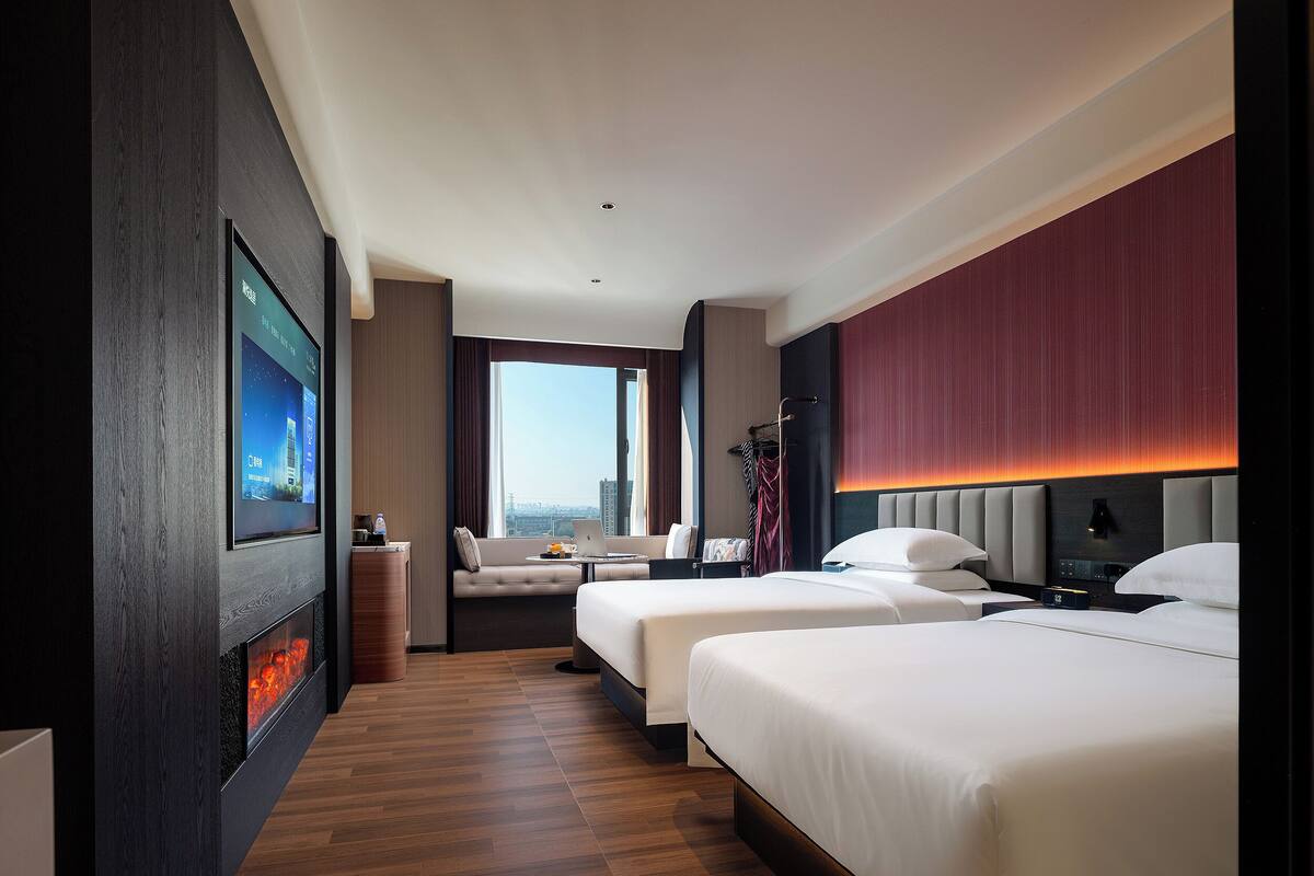 A hotel room with two beds, a sofa, a TV, and a fireplace.