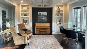Un salon avec une cheminée, un piano, un canapé, une table basse et un coin repas avec des chaises.