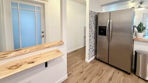 Uma cozinha moderna com geladeira de aço inoxidável, bancada de madeira e porta com painéis de vidro jateado.