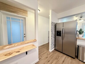 Una cuina moderna amb nevera d'acer inoxidable, taulell de fusta i una porta amb panells de vidre mat.
