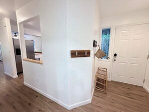 Un passadís amb una porta blanca, un sòl de fusta i una cistella penjada a la paret.