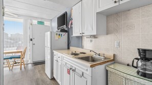 A kitchen with white cabinets, a stove, a sink, a microwave, and a glass coffee table. - Oceanview Condo Steps from Beach & Boardwalk in North Wildwood (Wildwood)