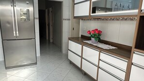 Una cocina con un refrigerador de acero inoxidable, un armario de madera con puertas de vidrio y suelo de baldosas.